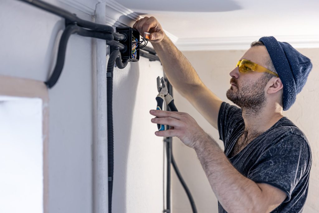 an electrician is mounting electric sockets on the white wall indoors scaled 1