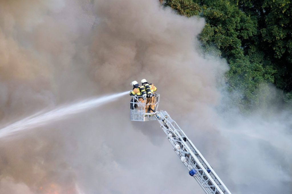 two firefighters trying to stop the fire in the forest surrounded by smoke scaled 1